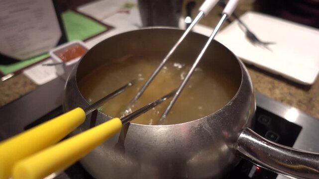 Boiling broth fondue pot with forks sitting in hot soup at a restaurant table.