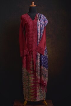 Maroon embroidered kebaya with batik skirt and shawl displayed on a dress form