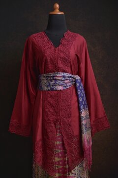 Maroon embroidered kebaya with batik skirt and shawl displayed on a dress form