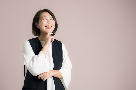 ピンク背景でオフィスカジュアルの考える悩む40代女性、笑顔のビジネスポートレート