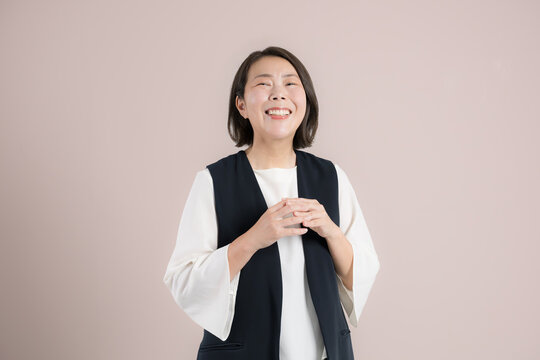 ピンク背景で目標達成を喜び笑顔で感謝するありがとうポーズ　成功と喜ぶを表現するポートレート楽しそうなお母さんのような40代の女性