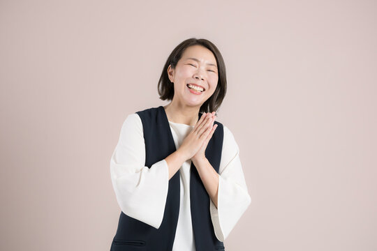 ピンク背景で目標達成を喜び笑顔で感謝するありがとうポーズ　成功と喜ぶを表現するポートレート楽しそうなお母さんのような40代の女性