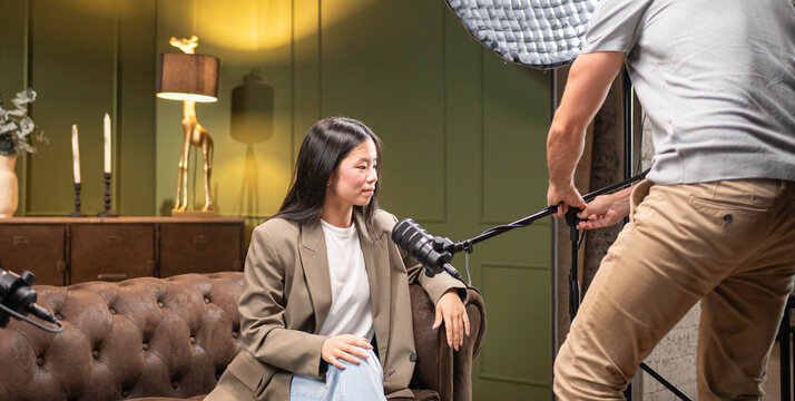 Woman sitting on couch for podcast with male engineer adjusting lighting in studio