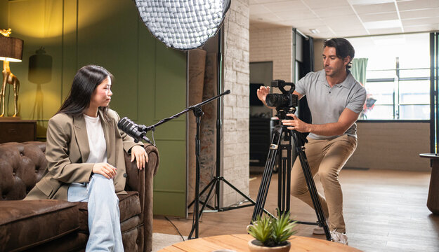 Woman sitting on a sofa recording a podcast, while a videographer films her
