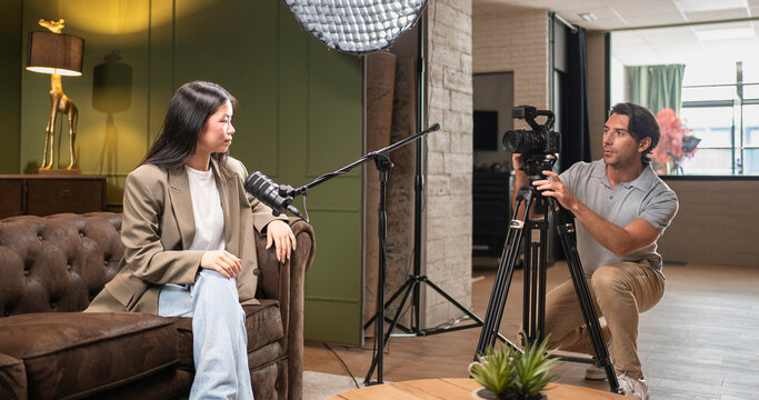 Young asian woman speaking into a microphone while man adjusts video camera