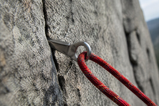 A steel climbing piton in granite with a rope, natural daylight.