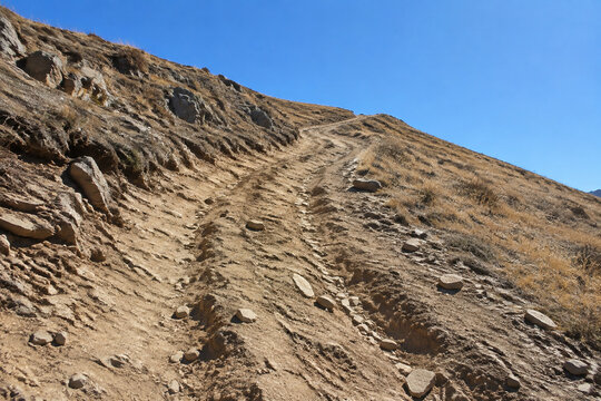 Steep unpaved trail on dry rocky hillside with ruts and exposed roots, arduous hiking path concept