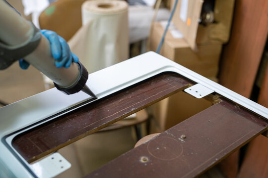 Hand applying sealant to white frame edge in workshop