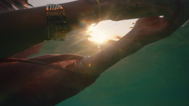 A flowing dress trails and billows in the water as a woman wades deeper into the sunset sea.