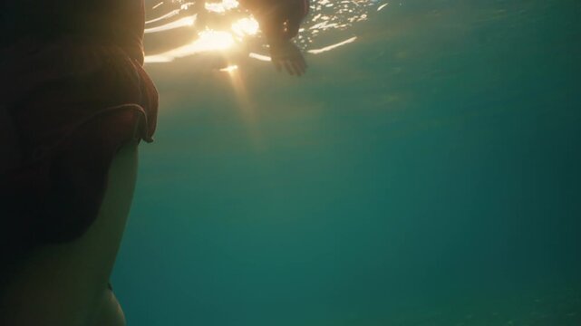 Underwater close up of a hand reaching upward as bright sunlight streams through the water.