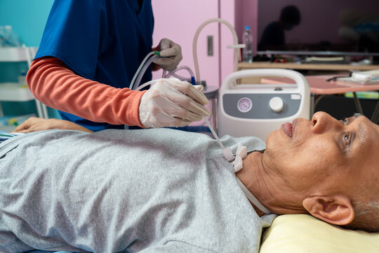 Asian nurse suctions mucus from a tube in the throat of a patient who had a tracheostomy and is recovering at home