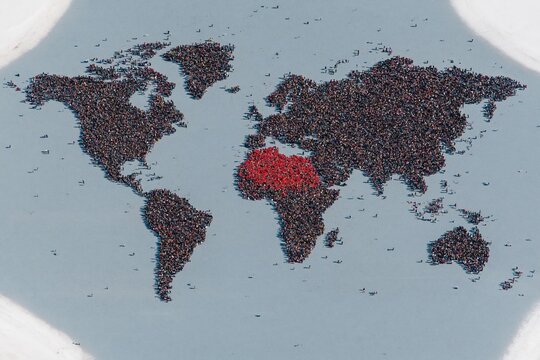 World map formed from miniature figures on a smooth grey surface, featuring a red cluster to highlight population density for demography and global development