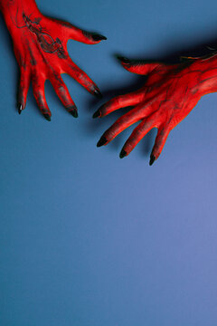 Halloween. Red hands with sharp black nails reach out against blue background