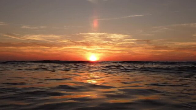 Golden sunset reflecting on ocean water ripples at horizon level