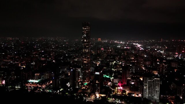 Drone orbit moves right to left around The 42 at night in Kolkata, keeping the illuminated landmark centered against the city skyline.