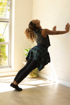 African woman leaning back against white wall at home near louvers, flannel shirt tied at waist