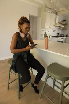 African woman sitting at kitchen, wearing tank, leggings, using phone near pink bottle