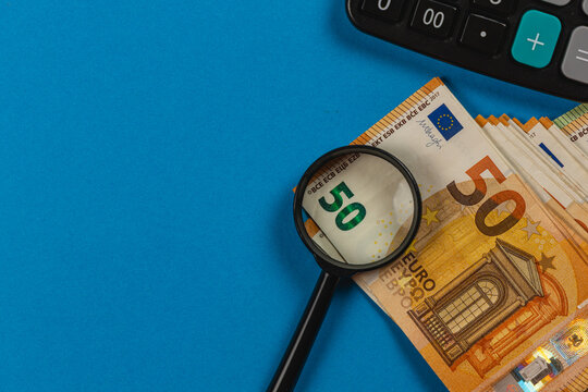 Magnifying glass on euro banknotes next to a calculator