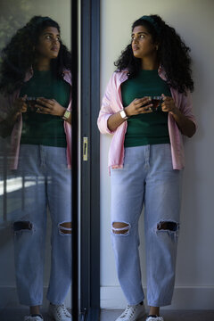 Indian woman standing by sliding glass door at home holding clear glass cup, copy space