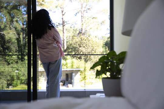Adult female wearing pink top and blue pants standing at sliding glass door with potted plant