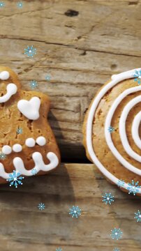 Snowflakes falling against gingerbread man cookies and candy cane on wooden surface