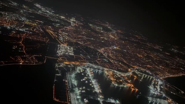 Cockpit night view of Valencia city while flying over the harbor in a left turn, with the illuminated airport runway at the back.