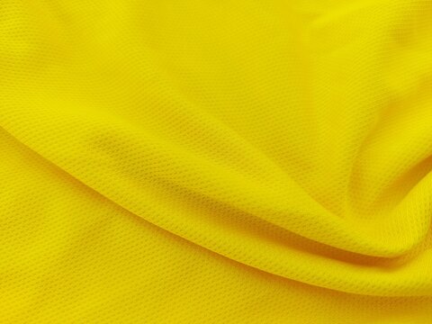 Yellow football jersey clothing fabric with smooth textile texture. Close up sports wear background with soft yellow fabric detail. Football shirt jersey material texture.