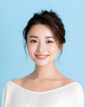 美容広告に最適な、なめらかな美肌の日本人女性。淡いブルーの背景で自然な笑顔を見せるまとめ髪のポートレート