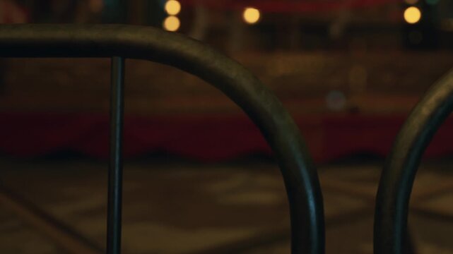 The scene shows metal bars in front of a dimly lit room. Soft lights create a low ambiance. The area appears abandoned and quiet with a few objects visible beyond the bars.