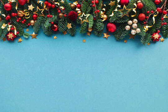 Festive Christmas and New Year flat lay composition with fir branches, colorful ornaments, red berries, confetti strars decoration on blue background top view.