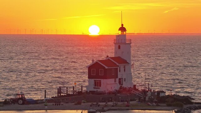 Beautiful sunset over the historic paard van marken lighthouse. The sun dips below the horizon, casting a warm orange glow on the sea and landscape