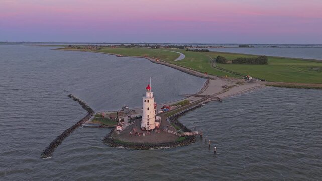 Dramatic aerial orbit revealing the historic paard van marken lighthouse in the netherlands against a beautiful pink and purple sunset sky