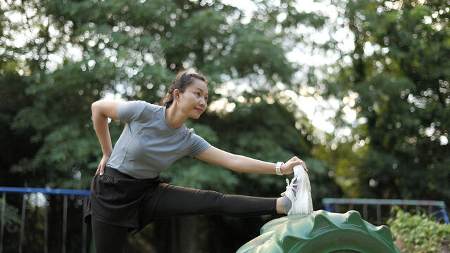 Young Asian Woman Doing Hamstring and Leg Stretch on Tire in Green Playground Park Fitness Concept 4K