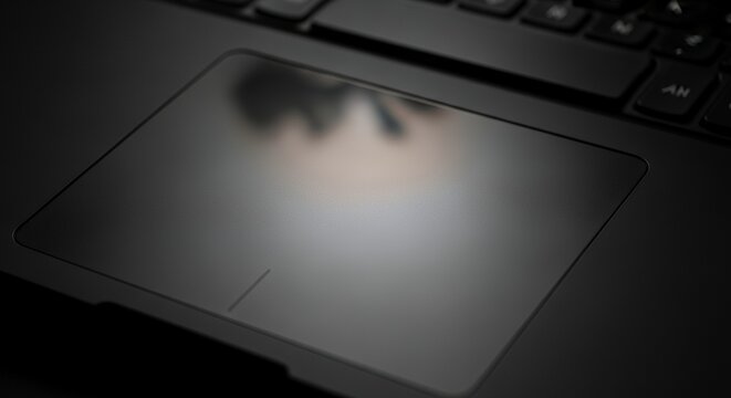Close-up of a laptop touchpad in a dimly lit environment, highlighting its sleek surface and subtle reflections.