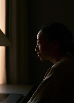 Silhouette of a woman sitting in front of a window. she is facing away from the camera, with her head turned slightly to the side.