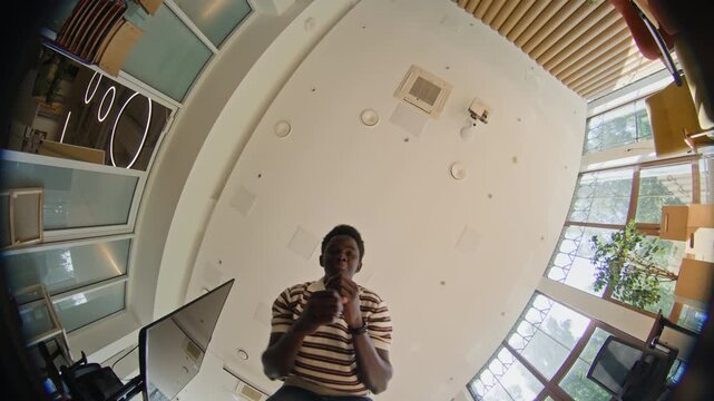 Portrait of African American young adult man dancing and gesturing playfully in modern office, captured from low angle fisheye POV. Footage is ideal for corporate culture and HR marketing campaigns