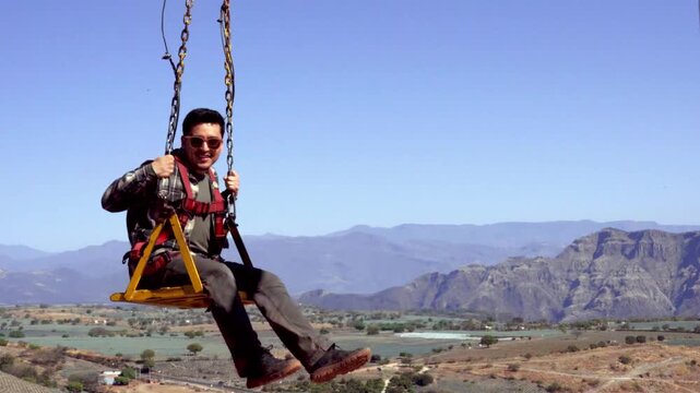 Man swinging at viewpoint overlooking valley and mountains under clear blue sky
