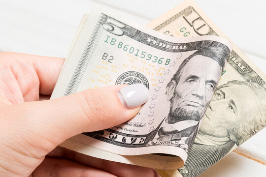 A pack of five and ten dollar bills in female hand on wooden background. Salary concept with copy space