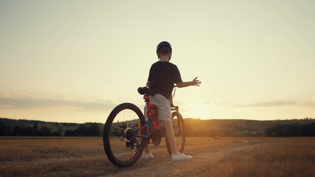 Little child learning to ride bike in country, back view of boy on bicycle. Merry childhood moments, carefree preteen spending summer weekend in nature, active lifestyle, children play outdoors