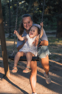 Cheerful mother pushing her laughing little daughter on a swing.