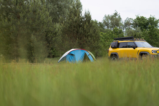 Yellow electric SUV and tent pitched in a grassy field