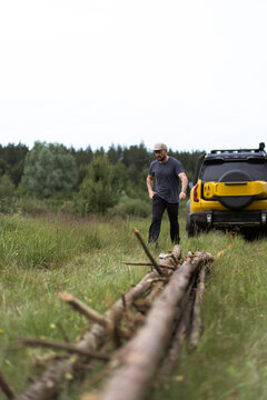 Man surveys a pile of logs near his yellow suv