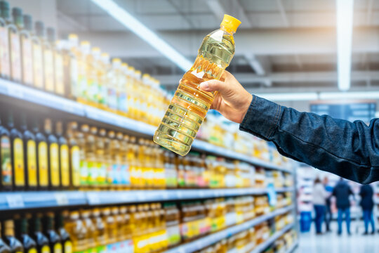 Shopper holding a bottle of cooking oil while choosing products in a bright supermarket aisle with blurred shelves in the background.