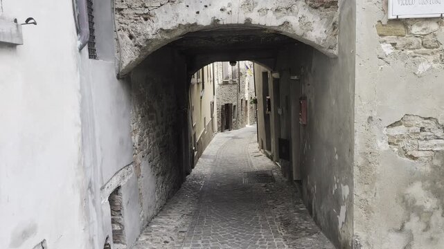 Inquadratura di un tipico passaggio coperto ad arco in pietra situato nelle strette vie acciottolate del centro storico di Sassocorvaro, nelle Marche.