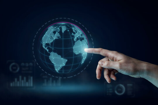 A human finger touching a glowing digital globe interface with data charts and network connections on a dark blue background screen