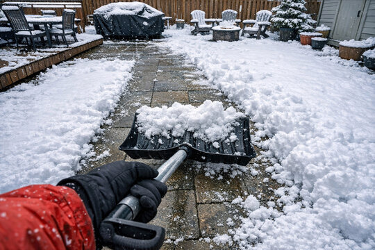 A person using a shovel to clear snow off a garden path in the aftermath of a snowstorm.