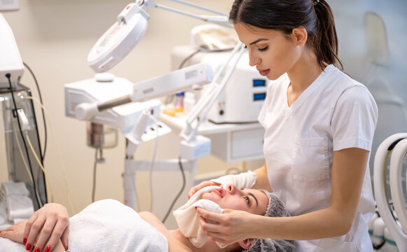 Professional aesthetician cleansing female client face with warm towel after mask