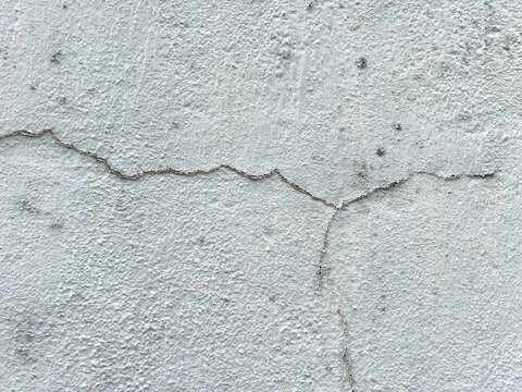 Close-up texture background of a thin hairline crack splitting on a rough white stucco wall.