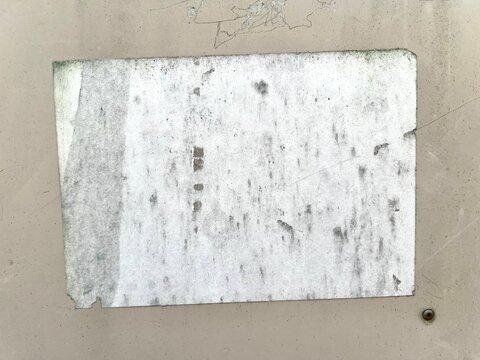 A blank weathered white paper poster stuck on a smooth beige metallic panel surface.