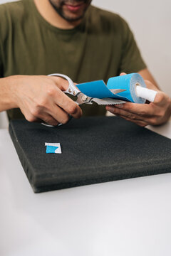 Vertical cropped shot of man cutting preparing kinesiology tape roll, providing support and pain relief for muscle injury or joint problems, showcasing sports medicine and physiotherapy treatment.